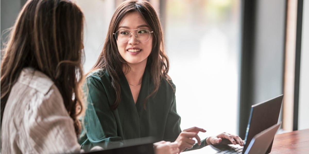 two asian ladies having a conversation in the office with laptops