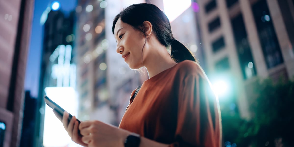 Woman standing outside smiling down at her phone